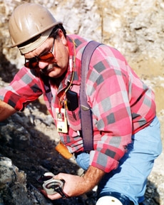GEOLOGIST TAKING FRACTURE MEASUREMENTS AT EXPLORATORY STUDIES FACILITY, NORTH FACE.
YUCCA MOUNTAIN, ON SOUTHWEST BOUNDARY OF NEVADA TEST SITE, EVALUATED FOR NATION'S FIRST REPOSITORY FOR COMMERCIAL HIGH-LEVEL RADIOACTIVE WASTE. GEOLOGICAL, HYDROLOGICAL & GEOPHYSICAL DATA OBTAINED FROM EXPLORATORY HOLES DRILLED AROUND THE MOUNTAIN. WATER TABLE AT YUCCA MTN. IS 1700 FT. DEEP, PERMITS CONSTRUCTION OF A REPOSITORY SOME 700 FT. ABOVE STANDING WATER IN AN UNSATURATED ZONE. YUCCA MTN.- ONE OF THE MOST ARID & MOST SPARSELY POPULATED REGIONS IN U.S. 
Keywords: Yucca Mountain Site Characterization